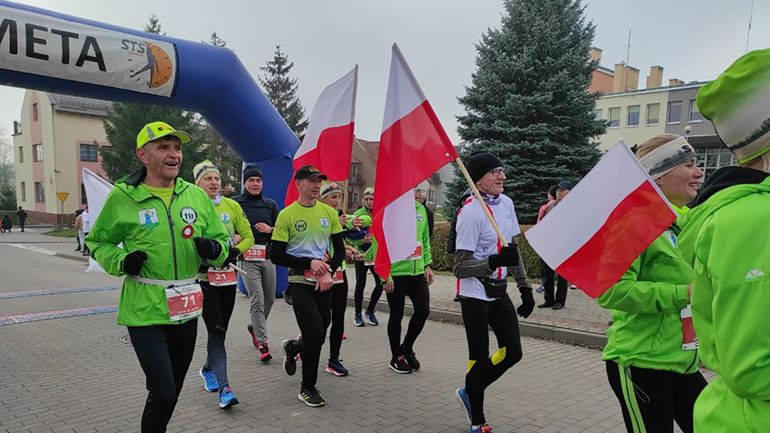 Zdjęcie przedstawiające biegaczy z biało-czerwonymi flagami wbiegającymi na metę 